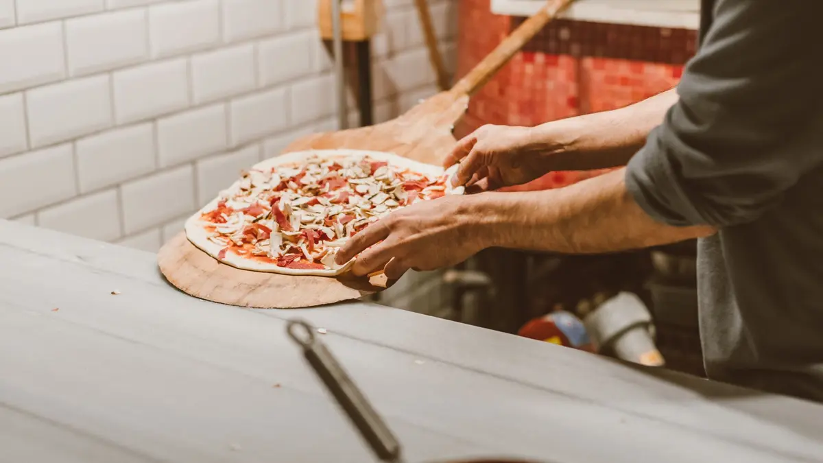 Belegde pizza op een houten pizzaschep, klaar om de oven in te gaan