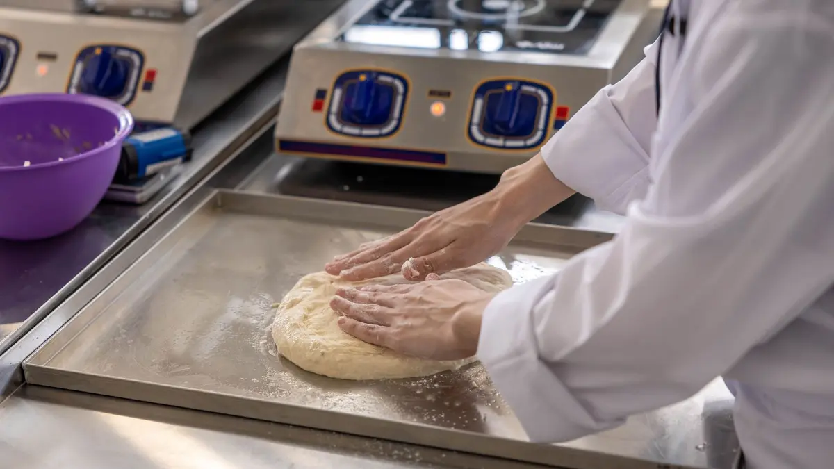 Handen die deeg kneden op een roestvrijstalen werkblad